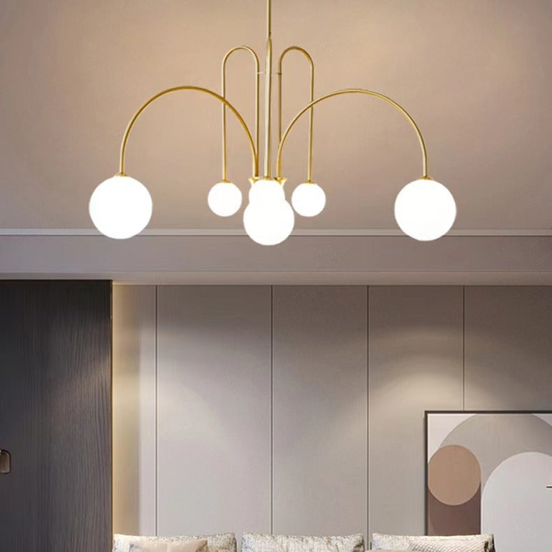 The St Kilda Chandelier, featuring a gold frame and five white globe lights, hangs from the ceiling. The rooms neutral walls complement abstract wall art, with a glimpse of a sofa below.