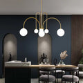 In a modern dining room, the St Kilda Chandelier with five globe lights hangs over a table adorned with two black vases. Dark walls, arched niches, and tall wood paneling accentuate the rooms elegance.