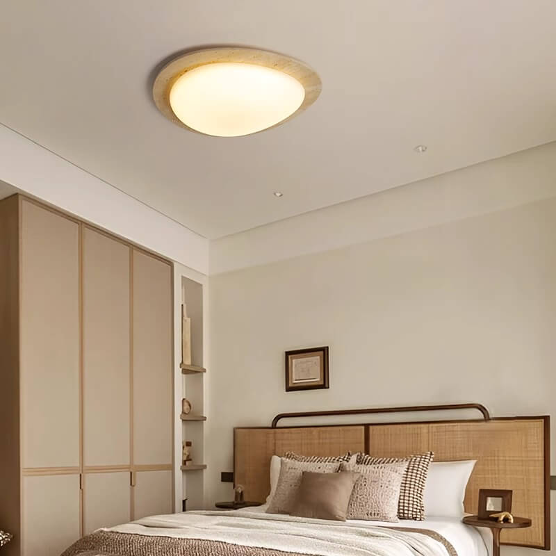 A cozy bedroom with a large bed, earth-toned pillows and blanket, wooden headboard, built-in wardrobe, and wall shelves. Natural travertine accents and the Wabi-Sabi Travertine LED Ceiling Light create a minimalist warmth.