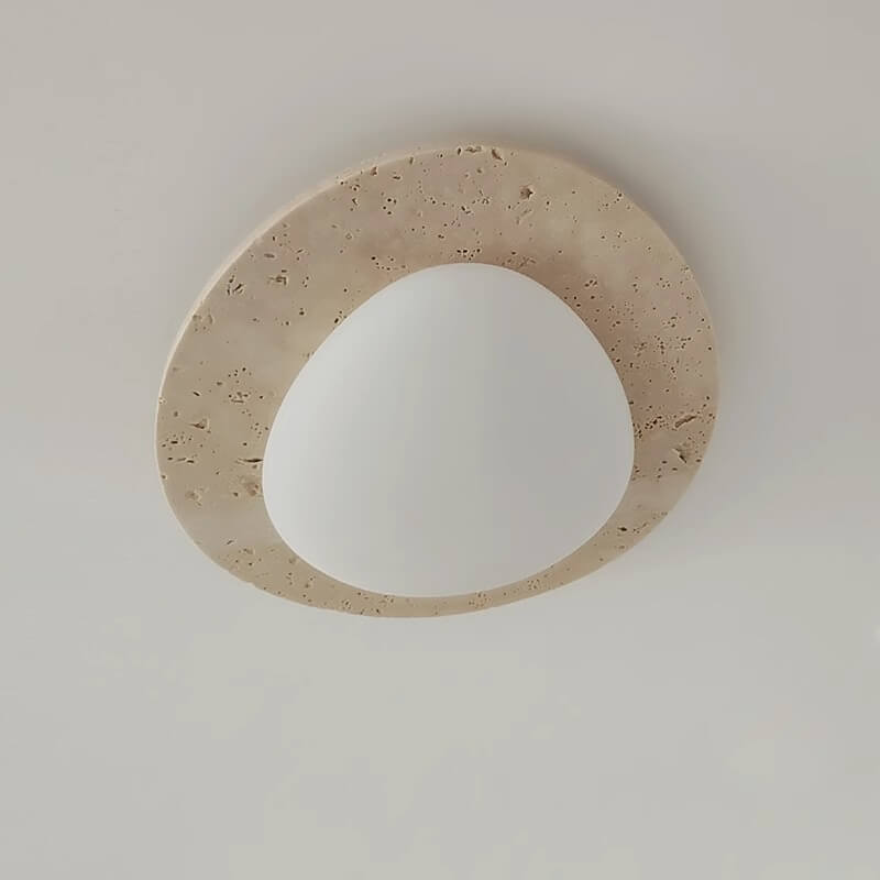The Wabi-Sabi Travertine LED Ceiling Light features an irregular oval shape with a smooth white center, bordered by a beige travertine stone-like texture inspired by Wabi-Sabi design.
