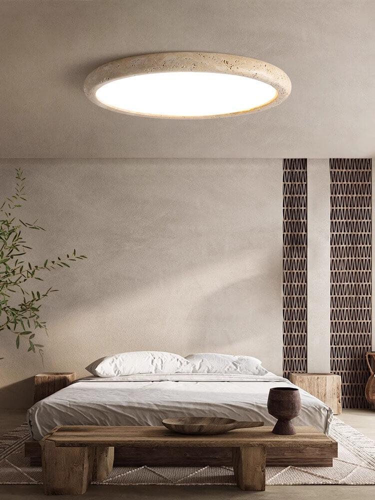 Minimalist bedroom with a low wooden bed, white bedding, small wooden side table, geometric wall art, leafy plant, and a large Travertine Ceiling Light. Neutral tones and natural style create a calm, serene atmosphere.