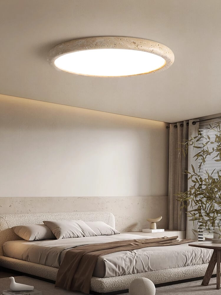 Minimalist bedroom with a low wooden bed, white bedding, small wooden side table, geometric wall art, leafy plant, and a large Travertine Ceiling Light. Neutral tones and natural style create a calm, serene atmosphere.