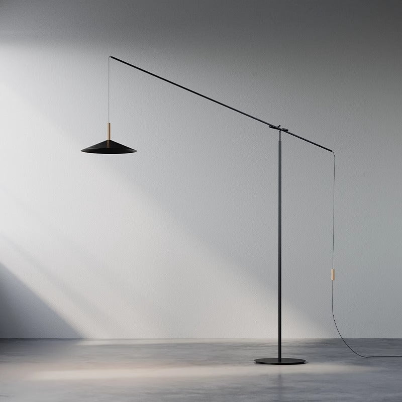 The Velluto Floor Lamp boasts a minimalist design with an adjustable arm and cone-shaped shade, casting a warm glow on neutral gray walls, while its slender form adds elegant simplicity to any room.