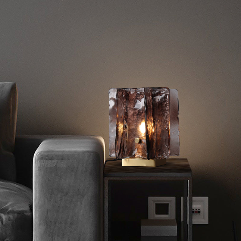 A modern living room with grey walls highlights a dark grey sofa paired with a Vintage brass glass table lamp. Its wavy, hand-blown amber glass shade casts a soft glow, enhancing the chic and cohesive ambiance.