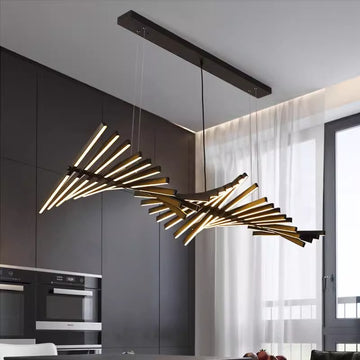 The Fishbone Wave Chandelier, with adjustable staggered linear elements, emits a warm glow. Perfect for a contemporary kitchen with dark cabinetry and built-in ovens, its elegant design and superb customization options complement a large window draped in sheer curtains.