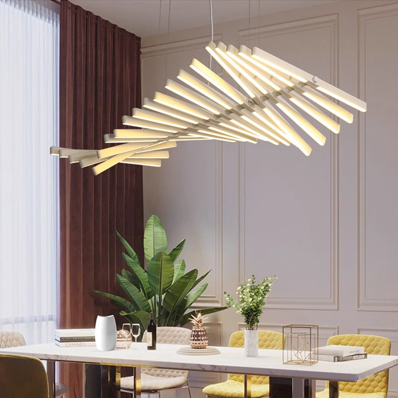 A modern dining room showcases the Fishbone Wave Chandelier with adjustable lighting over a table adorned with decorative items, including a white vase and golden pineapple. A plant and red curtains by the large window enhance elegance, while light-colored walls offer chic customization options.