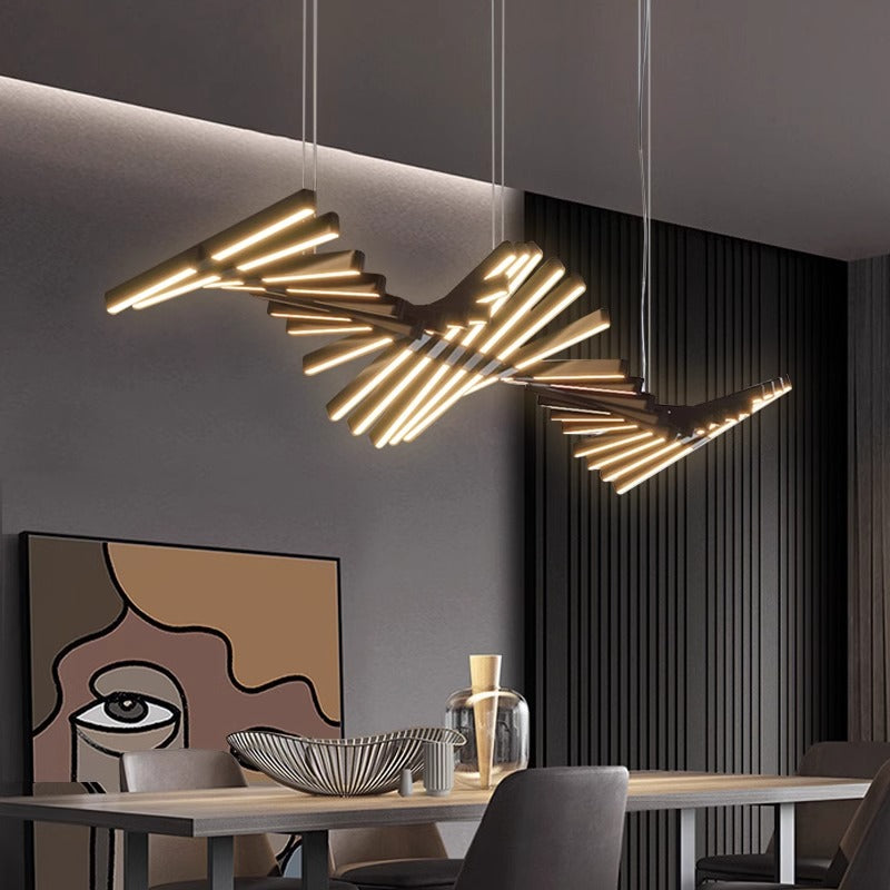 A modern dining room features the Fishbone Wave Chandelier, a unique piece with adjustable glowing horizontal rods. Below it, a table holds decorative items, while abstract face wall art contrasts beautifully against dark vertical paneling.