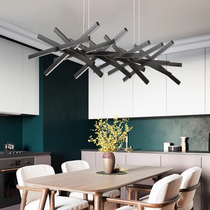 A modern kitchen features dark green and white cabinets. In the center, a wooden dining table is surrounded by cream chairs, topped with a yellow-flowered vase. Overhead, the Fishbone Wave Chandelier with crisscrossing rods provides adjustable lighting for custom options.