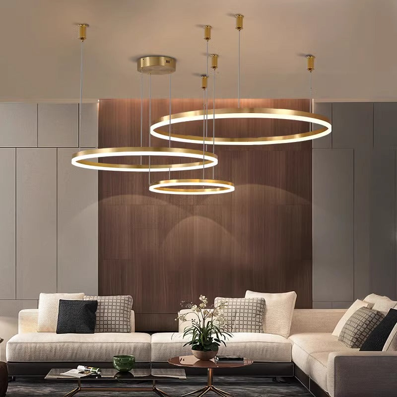 Modern living room with beige sectional sofa, green and gray cushions, wooden accent wall, and three circular pendant lights.