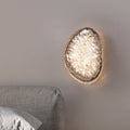 The wall lamps for bedroom feature a modern acrylic geode-like design. They mount above a gray upholstered headboard with a crystal-textured center, offer energy-efficient LED lighting, and smart dimming, adding an elegant ambiance to the room.