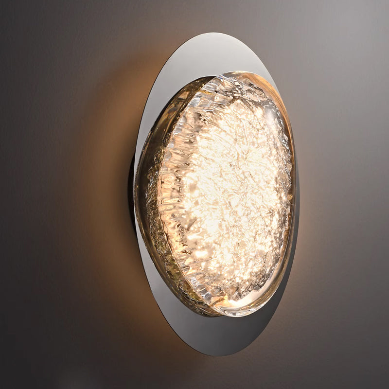 This wall lamp for the bedroom is a round, wall-mounted fixture with a textured glass center and energy-efficient LED technology. It emits a bright, warm glow that creates subtle shadows, while its smooth, reflective surface adds an elegant touch to this modern acrylic design.