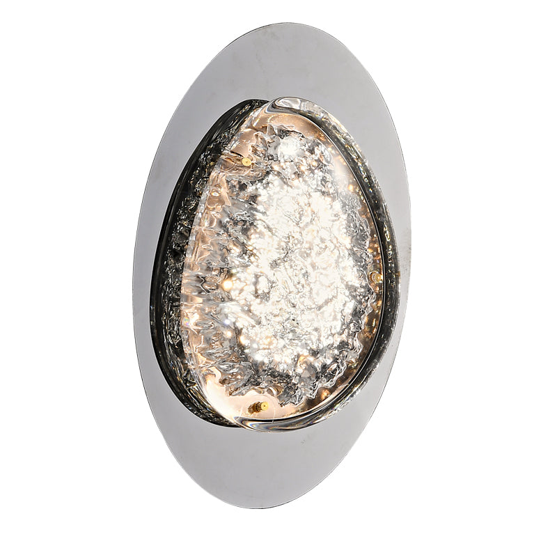 The oval-shaped silver wall sconce features a textured transparent glass center, emitting a warm glow with energy-efficient LED technology and smart dimming capabilities; great wall lamps for bedroom ambiance.