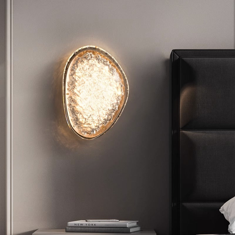 The wall lamps for bedroom offer a unique, modern acrylic design with an irregular oval shape that emits a warm glow. Featuring smart dimming, theyre mounted next to a dark upholstered headboard. Nearby, a small stack of books sits on a table amidst the minimalist decor that enhances their elegance.